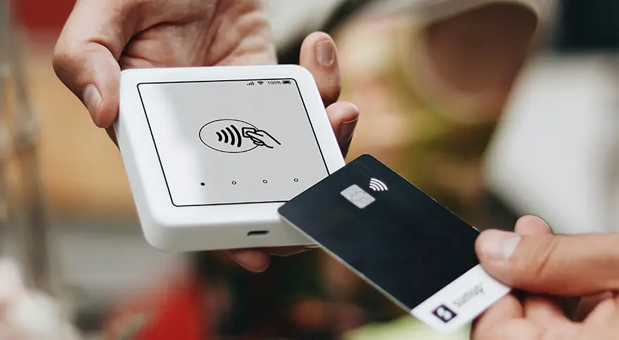 A hand holding a credit card to a contactless payment system.