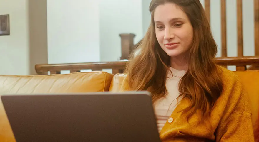 A young woman in sitting on a leather couch with a laptop.